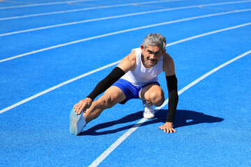 Senior Asian athlete doing stretching warm up for running in the professional blue track for...
