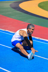 Senior Asian athlete doing stretching warm up for running in the professional blue track for professional exercise, sport training workout and healthy for longevity concept