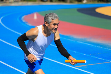 Senior Asian athlete is practicing running with relay baton in the professional blue track for professional exercise, sport training workout and healthy for longevity concept