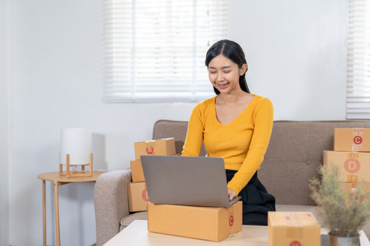 Young woman working on a laptop at home surrounded by packages, representing online shopping and e-commerce business.