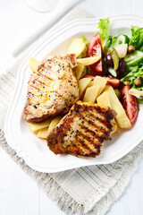 Grilled Steaks with french fries and fresh salad. Bright wooden background.	