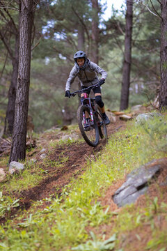 teen boy riding a mountain bike downhill through pine forest