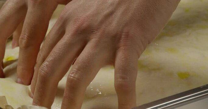 Close up of male hands dimpling a focaccia on a tray