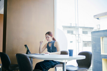 Young Woman Working on Tablet in Modern Cafe with Large Windows and Natural Light, Casual Work Environment, Remote Work, Freelancing, Contemporary Interior Design, Urban Lifestyle