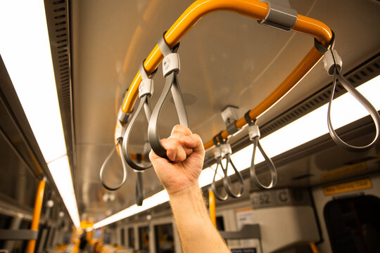 A person's hand holding onto a hand grip strap inside a commuter train