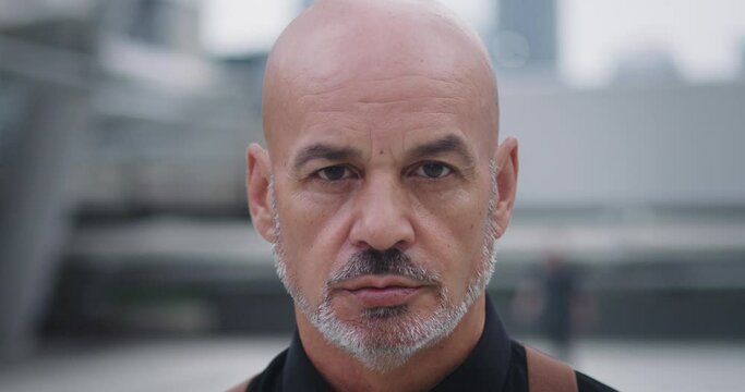 Close-up confident man with goatee and bald head looking straight into camera. Confident look and firm posture radiate strength and determination. Confident appearance impressive man attracts eye.