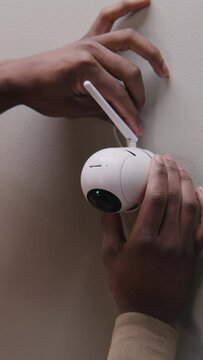 Vertical shot of African American man puts security camera on wall fastening and connects it to system with cable. Man installs cameras. Concept of CCTV cameras, monitoring system, safety and privacy.