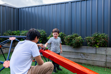 Chinese Australian dad playing with little boy in backyard racing trucks down ramp