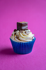 Chocolate bar cupcake with vanilla icing and chocolate sprinkles on pink background