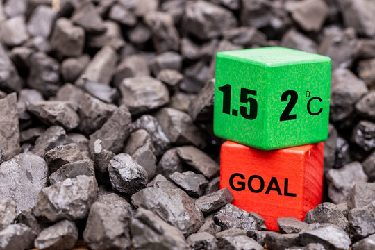 Symbol of reducing global warming among coal piles. A rotating wooden cube with the symbol "2 C" changing into "1.5 C" concept, reducing global warming or vice versa. reduction of fossil fuels