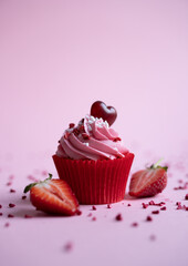 Delicious strawberry cupcake on pink background with sliced strawberry and heart candy