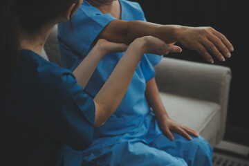 Obraz premium Old woman training with physiotherapist using dumbbells at home. Therapist assisting senior woman with exercises in nursing home. Elderly patient using dumbbells with outstretched arms.