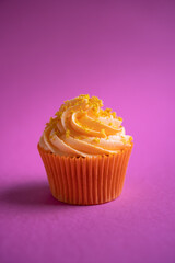 Delicious orange cupcake on pink background with orange zest