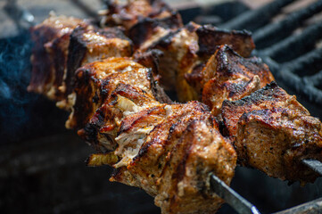 Grilled pieces of pork meat on metal skewers. Shashlik or shish kebab prepared on barbecue grill over hot charcoal with grilled vegetables.