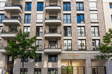A large building with many windows and balconies. The building is surrounded by trees and has iron gates.