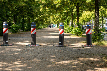 A row of four red and white poles with black tops are in a park. The poles are placed in a row,...