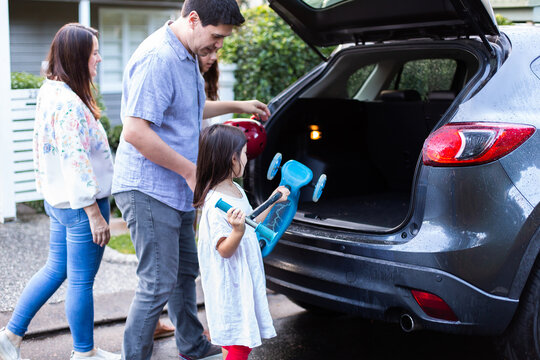 Two sisters with their mum helping dad get things loaded into the car for trip to park