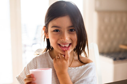 Close-up photo of a young girl smiling while holding a white cup at home with lost tooth