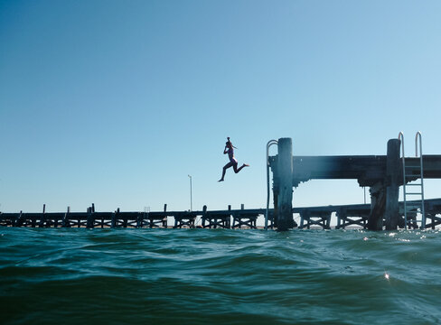 Girl jumping off jetty into ocean