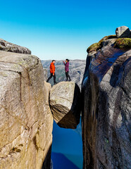 Two people stand on a rock bridge overlooking a stunning Norwegian landscape, seemingly suspended...