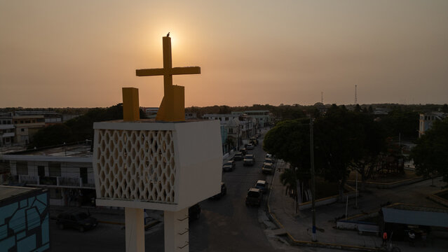 cruz catolica arriba en el campanario de un parroquia en corozal belice en centroamerica con el sol detras iluminando la cruz