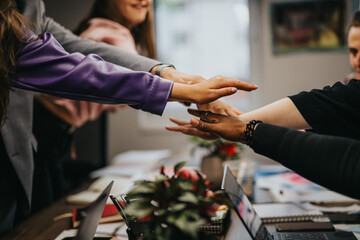 A dynamic office scene showing a group of coworkers joining hands together, symbolizing unity and teamwork during a brainstorming session at work.