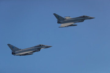 Two Typhoon Eurofighter jets flying over town centre with missiles on way to mission. Modern...