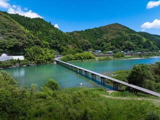 Fototapeta premium ドローン空撮。初夏、快晴の名越屋沈下橋と仁淀ブルー。高知県吾川郡いの町