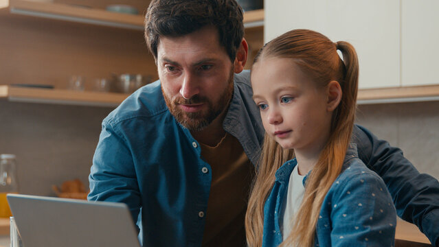 Happy family little daughter kid girl father checking homework helping cute school child with online studies laptop computer using at kitchen parent explaining distance learning at home education app