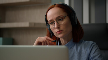 Caucasian business woman in headset communicate with clients solve problem female girl office worker conference video call with laptop computer. Serious businesswoman speaking talk webcam distant chat