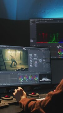 The editor works in studio on computer, uses color grading control panel, edits video, makes color correction for movie. Big screens showing program interface with film footage, RGB graphic and levels