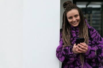 Street portrait of a young woman with piercings and African dreadlocks standing against a wall