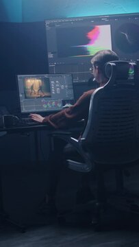 Female film editor or colorist does color grading on computer in modern studio. Big monitors with RGB colour correction graphic bar and program interface on the wall. Video post production. Handheld.