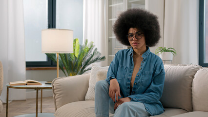 Serious confident ethnic girl African American woman at home sitting on couch sofa waving finger no...