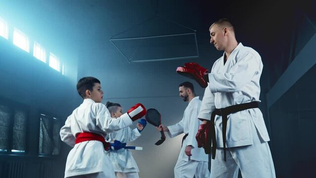 Group of young boys in martial arts class training leg attack. Children practice karate with trainer. Boy in kimono practicing punches. Instructors and children in karate class. 4K, UHD