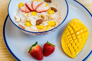 A bowl of oats with strawberries and mango arranged on a plate
