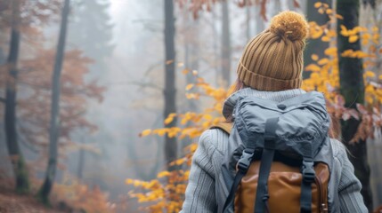 Foggy cold morning weather in autumn. Woman with backpack and knit hat hiking in forest at fall season