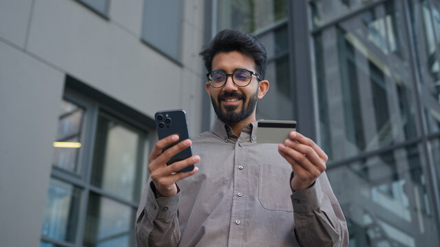 Happy Indian Arabian businessman use credit card online bank payment in city near office business customer entrepreneur man with mobile phone internet shopping buying easy pay money banking service