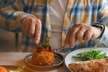 Person Using Fork to Eat Fried Arancini Ball Topped With Tomato Sauce and Basil