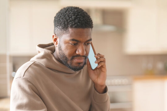 Serious Man Talking On Cell Phone In Kitchen At Home