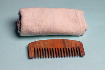 Extreme close-up of a Wooden comb and a properly folded towel kept on a sky blue background