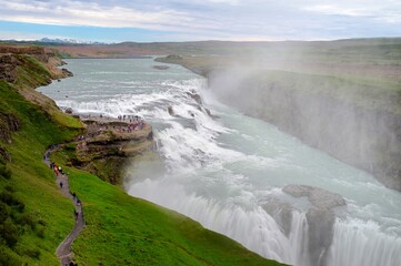 Tourists walking along the pat to view a wet Gullfoss waterfall