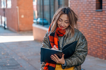 Woman Writing in Notebook on City Street in Autumn