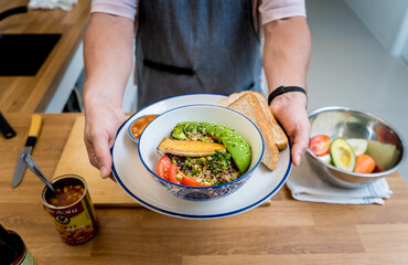 Chef at the kitchen preparing healthy quinoa bowl with avocado