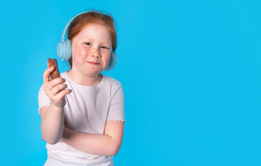 Young Girl With Red Hair Eating Chocolate Bar While Wearing Blue Headphones Against Blue Background