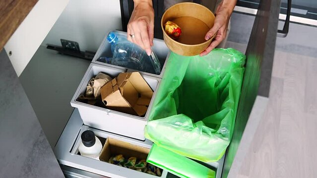 Hand of woman throwing trash into household bins for waste sorting in the kitchen for recycle. Plastic, paper, bio and mixed waste. Sorting waste at home concept