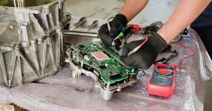 Mechanic Repairing Electronic Control Unit of Electric Car. Auto mechanic working on the electronic control unit (ECU) of an electric car. Technician testing and repairing the circuit board with tools