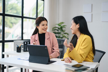 Obraz premium Two Professional Women Collaborating in Modern Office Setting with Laptops and Documents, Engaging in Productive Conversation, Business Meeting, Teamwork, and Corporate Environment