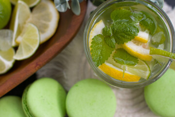 citrus lemon drink with lime in a glass, mint and ice and dessert macaroni cake. Refreshing drink, freshly squeezed refreshing juice