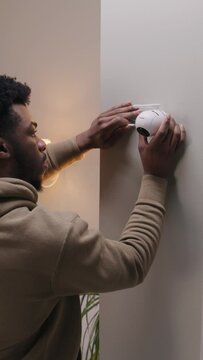 African American man puts security camera on wall fastening and connects it to system with cable. Man installs cameras in his apartment. Concept of CCTV cameras, tracking system, safety and privacy.